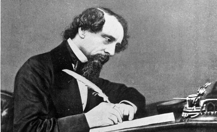 Photo of Charles Dickens writing at a desk with a quill pen